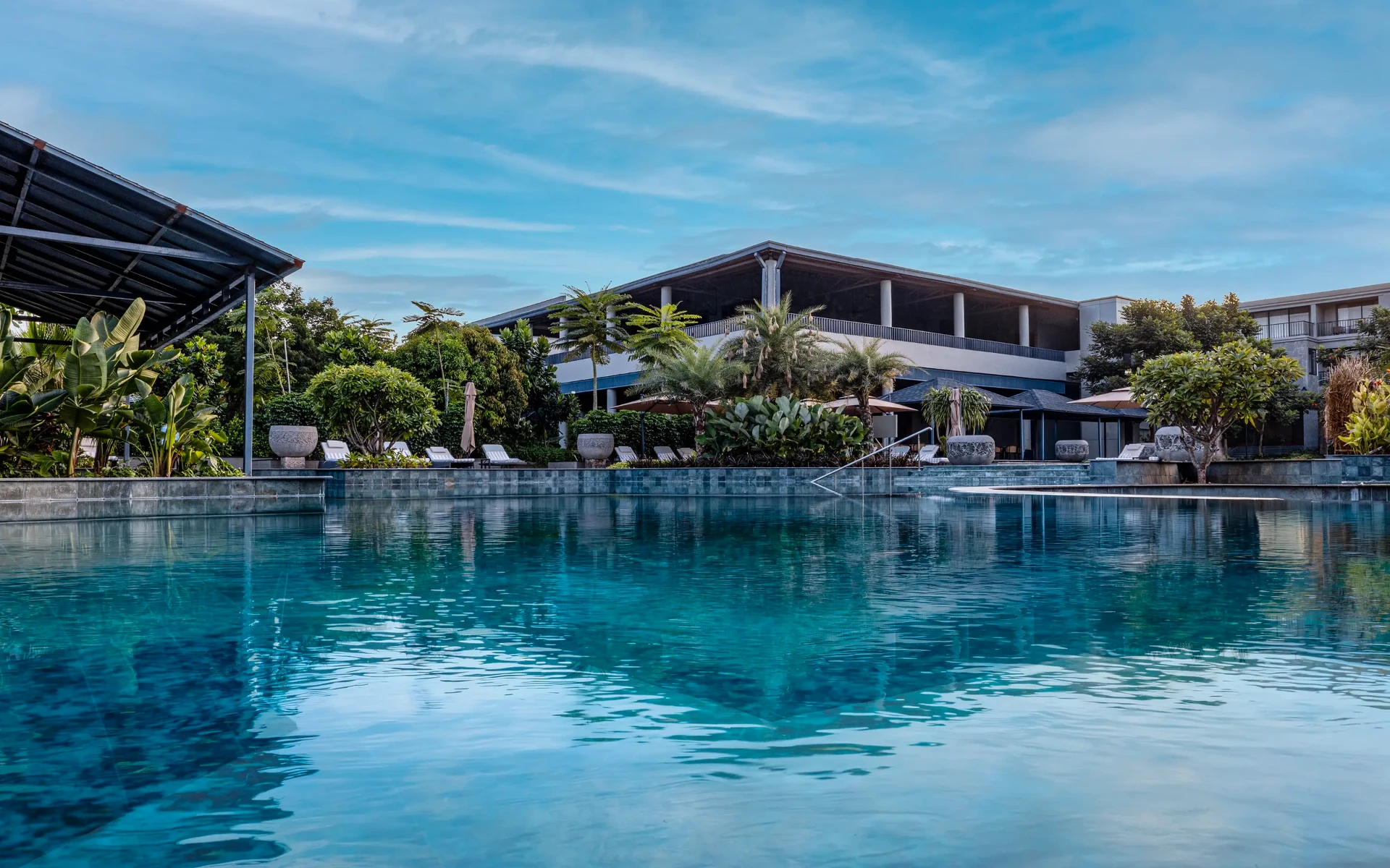 The estate's broad blue pool with greenery and resort architecture beyond